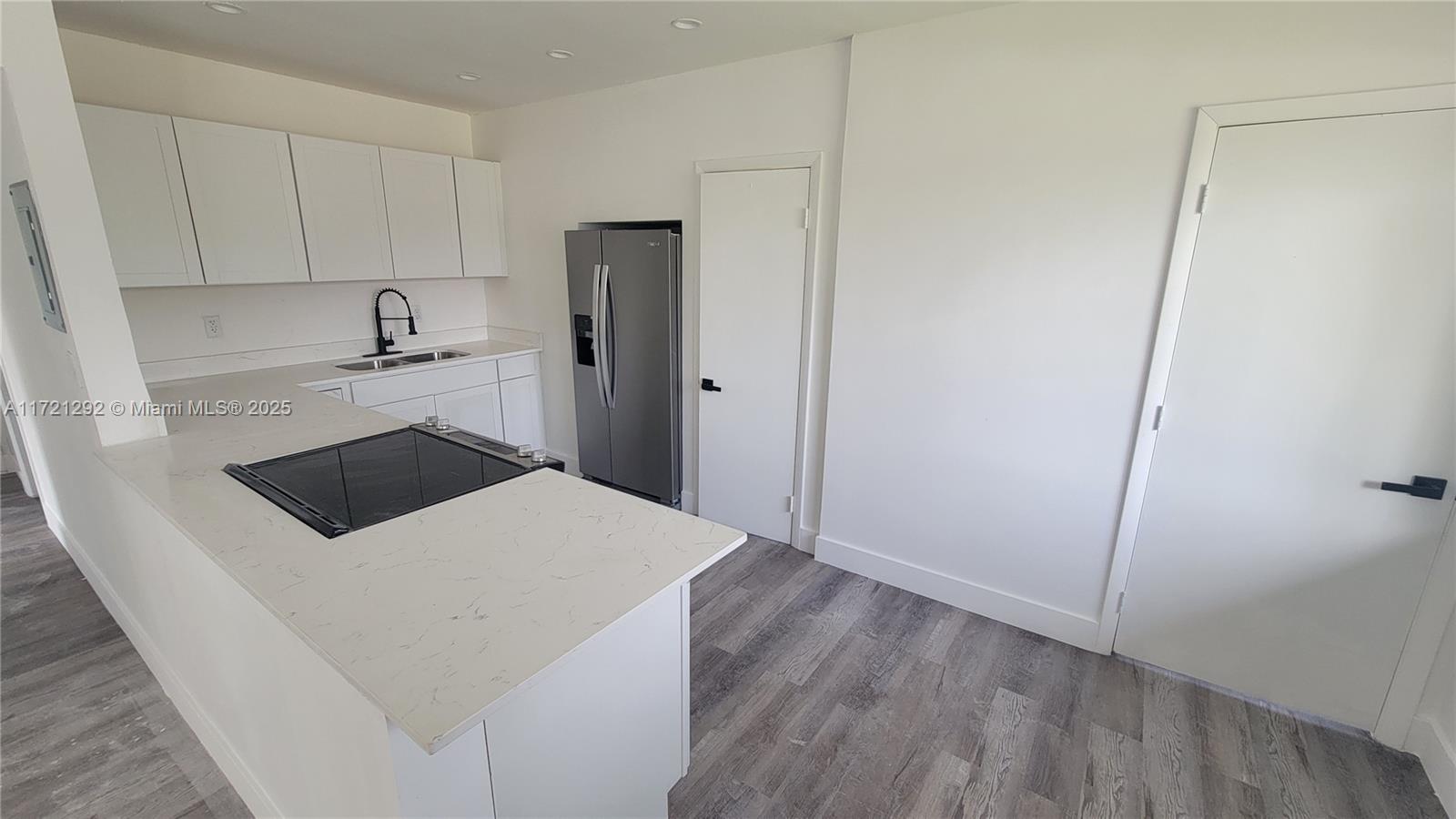 A kitchen features white cabinets, a quartz countertop, a stainless refrigerator, and gray flooring — 1560 NE 42nd Ct, Pompano Beach FL 33064, POMPANO BEACH, FL