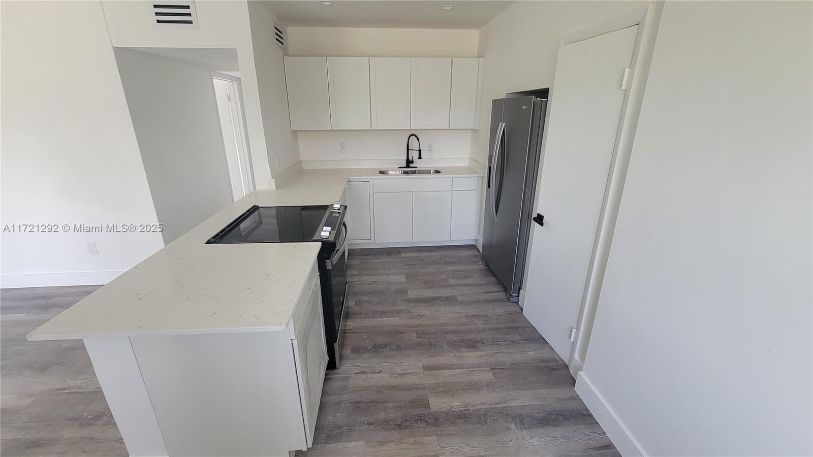 A kitchen features white cabinets, light countertops, stainless steel appliances, and gray wood-look flooring — 1560 NE 42nd Ct, Pompano Beach FL 33064, POMPANO BEACH, FL