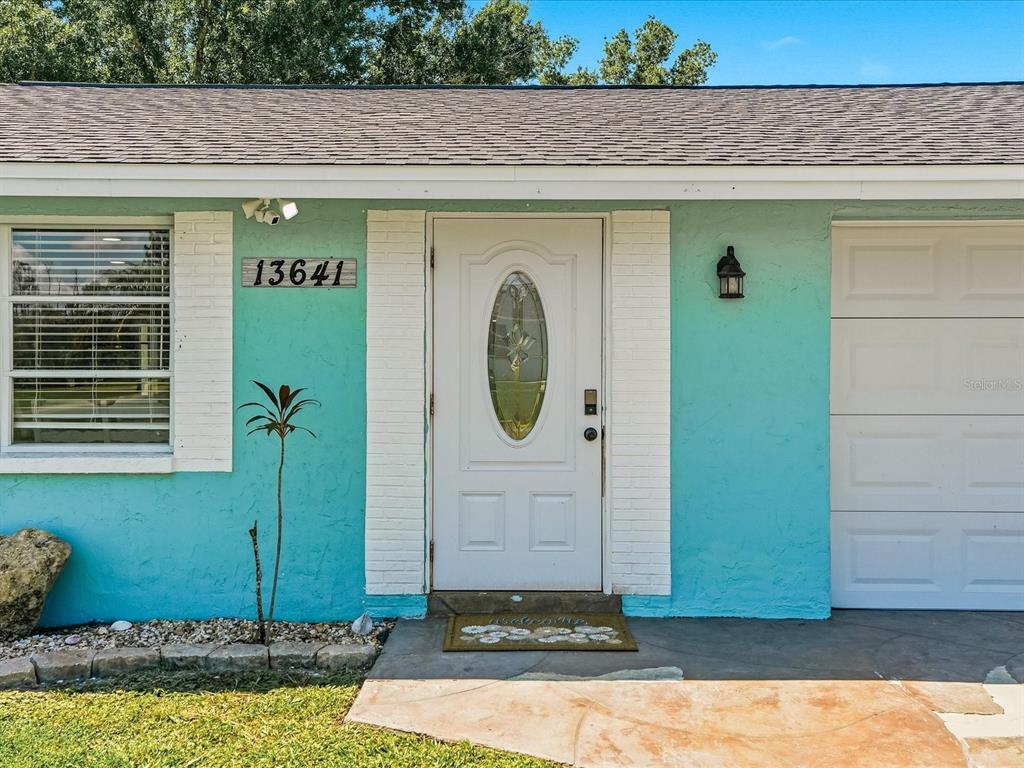 The exterior of a house features a teal painted wall, a white front door, and a window — 13641 DRYSDALE AVENUE, PORT CHARLOTTE, FL