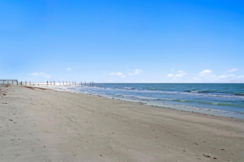 A sandy beach stretches toward the ocean under a clear blue sky with a pier — 16332 GULF BOULEVARD UNIT 3B, REDINGTON BEACH, FL