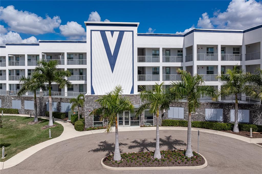 An exterior view of a multi-story apartment building with a large V logo — 1425 PARK BEACH CIRCLE UNIT 132, PUNTA GORDA, FL