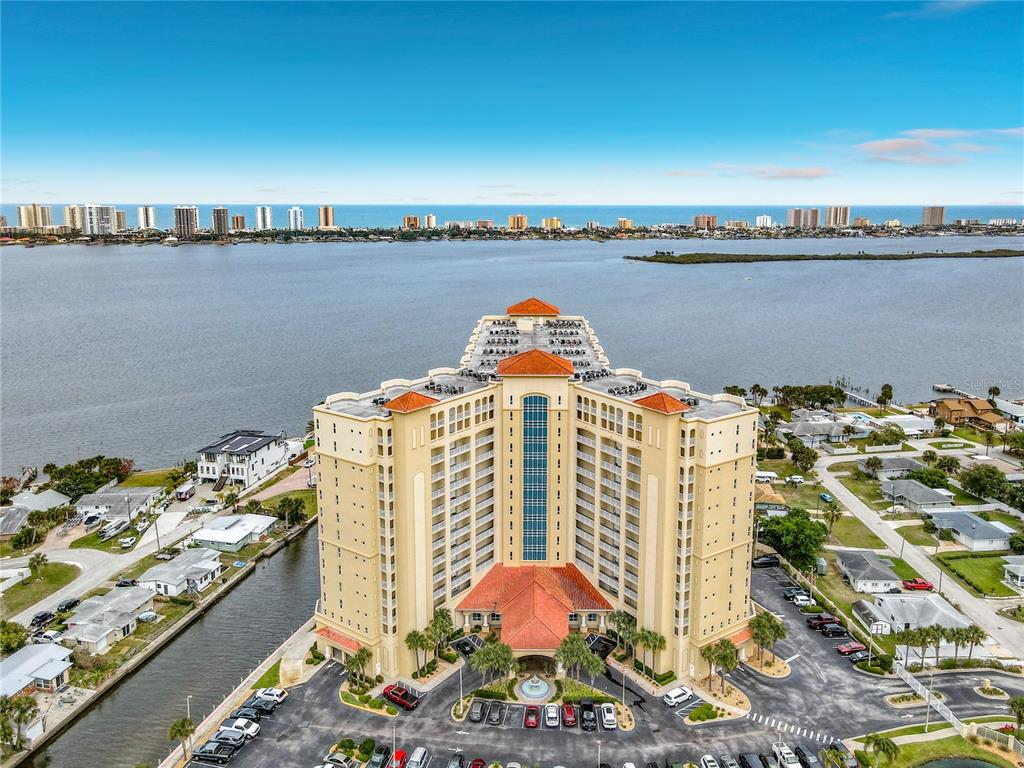 An aerial view shows a tall, tan residential building situated on a waterfront peninsula — 2801 S RIDGEWOOD AVENUE UNIT 1111, SOUTH DAYTONA, FL