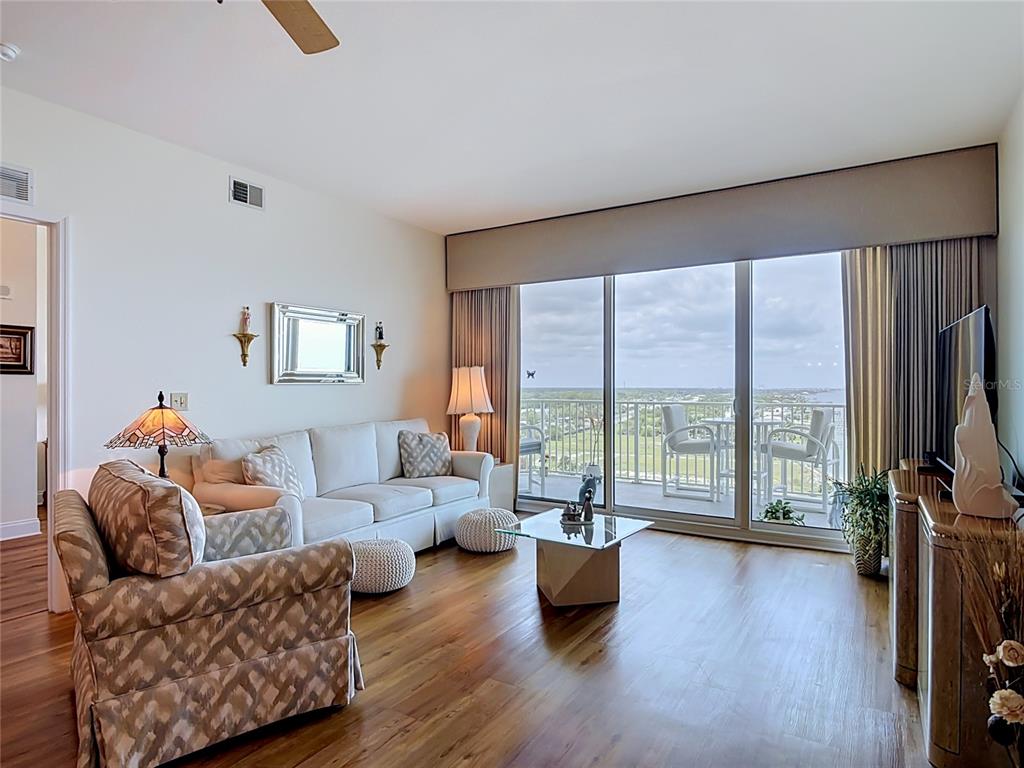 A living room features hardwood floors, a white sofa, patterned armchair, and a balcony view — 2801 S RIDGEWOOD AVENUE UNIT 1111, SOUTH DAYTONA, FL
