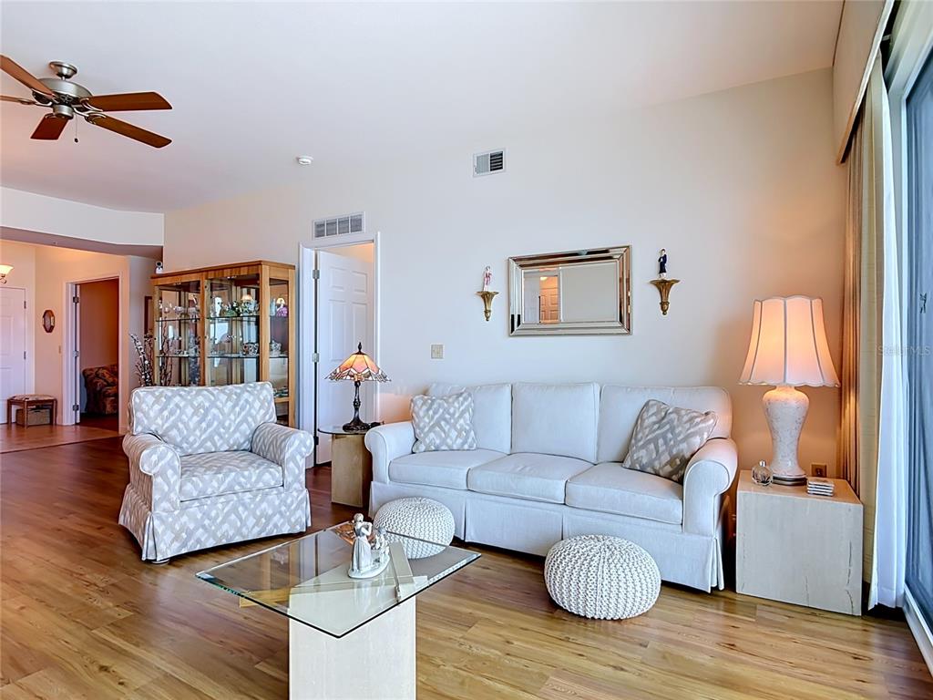 A living room features a white sofa, patterned armchair, glass coffee table, and hardwood floors — 2801 S RIDGEWOOD AVENUE UNIT 1111, SOUTH DAYTONA, FL