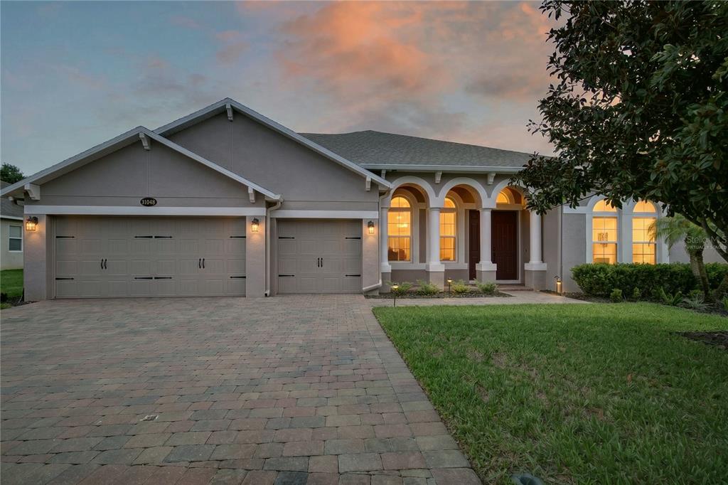 A single-story house with a three-car garage and arched entryway at dusk — 31948 GEOFF WAY, SORRENTO, FL