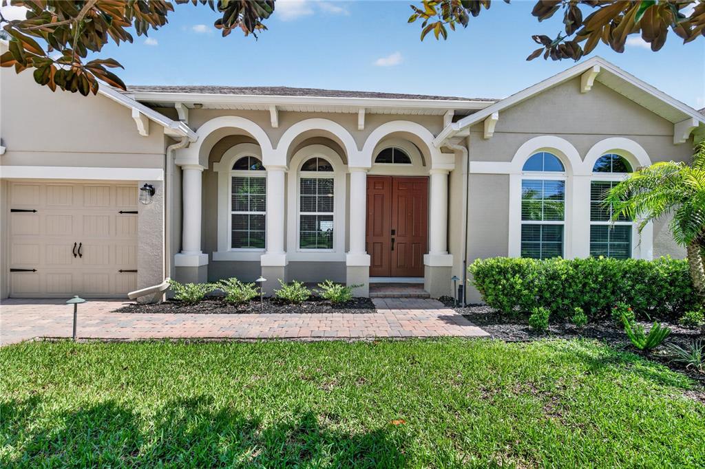A single-story house exterior features a tan stucco facade, arched windows, and a double-door entrance — 31948 GEOFF WAY, SORRENTO, FL