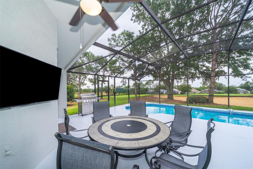 A covered patio features a dining set, a wall-mounted television, and a screened-in swimming pool — 1430 PARK PLACE, HAINES CITY, FL