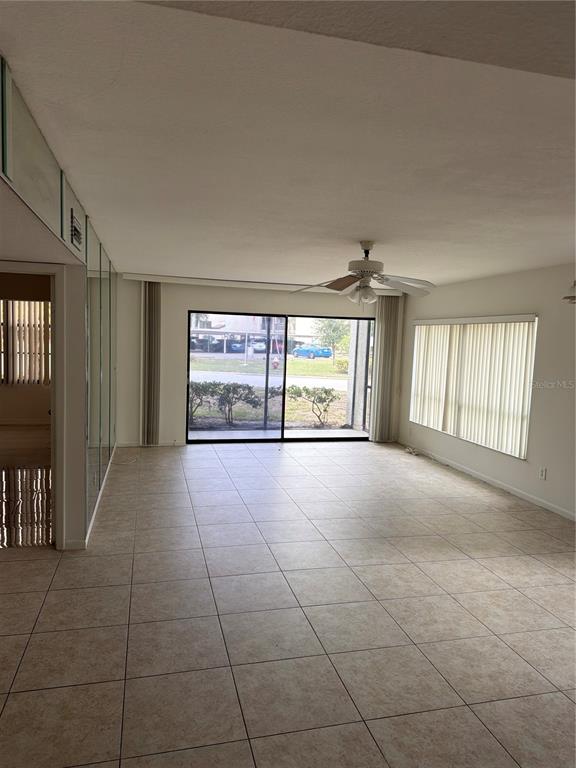 An empty living room features beige tile flooring, a ceiling fan, and large sliding glass doors — 700 STARKEY ROAD UNIT 1311, LARGO, FL