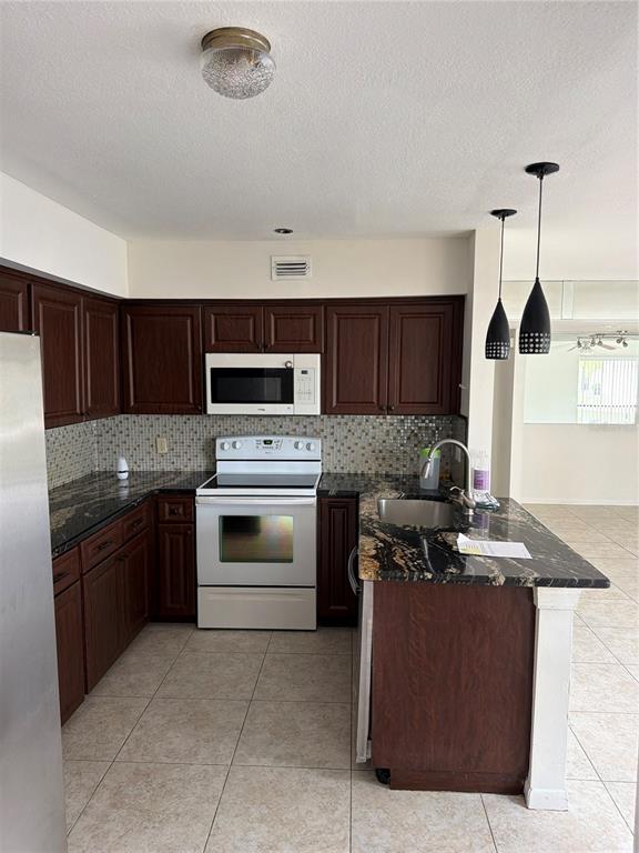 A kitchen features dark wood cabinets, granite countertops, a tiled backsplash, and stainless steel appliances — 700 STARKEY ROAD UNIT 1311, LARGO, FL
