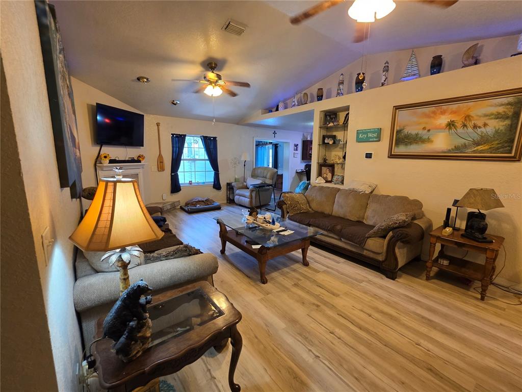 A living room features light wood-look flooring, a beige sofa, a coffee table, and ceiling fans — 5911 SE 127TH PLACE, BELLEVIEW, FL