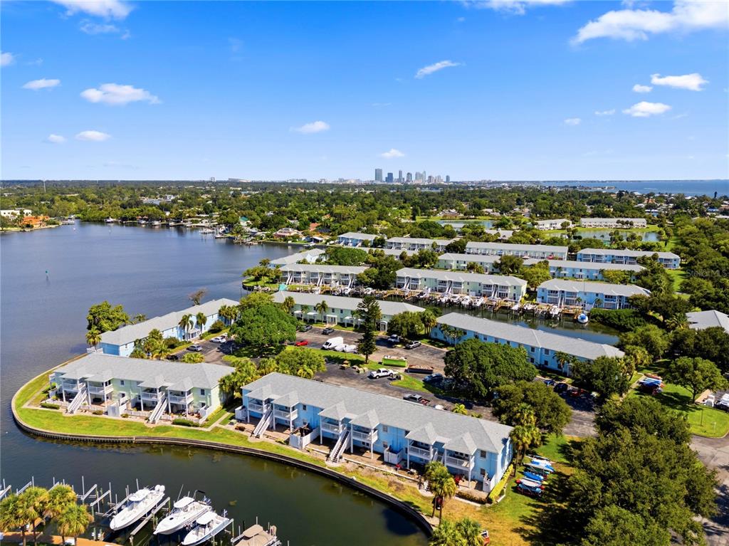 An aerial view of a waterfront condominium complex with boat slips and a distant city skyline — 5191 SALMON DRIVE SE UNIT D, ST PETERSBURG, FL