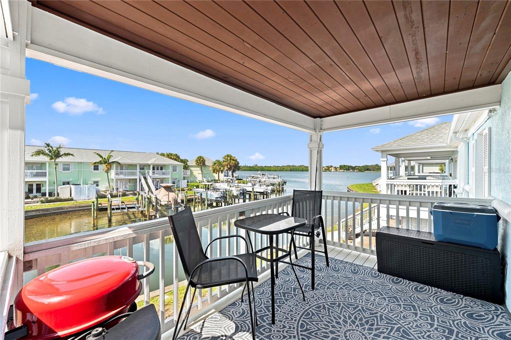 A covered balcony features a small table, two chairs, a red grill, and water views — 5191 SALMON DRIVE SE UNIT D, ST PETERSBURG, FL