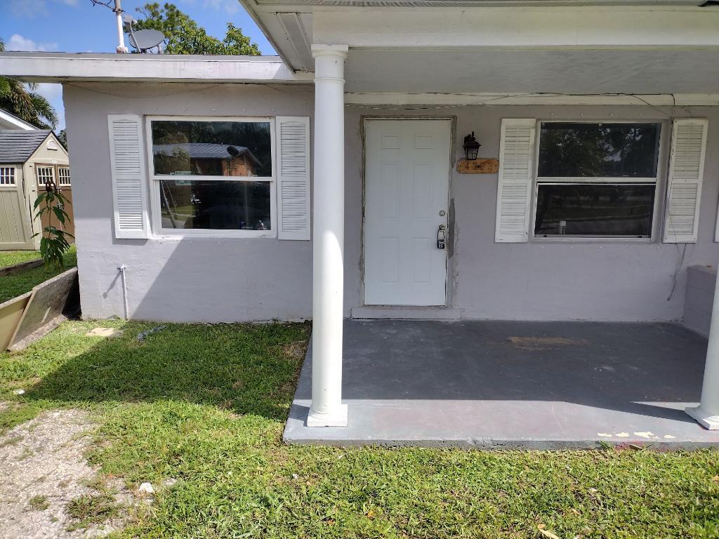 A gray house exterior features a front porch, white door, and two windows with shutters — 4383 SE Field Street, Stuart FL 34997, STUART, FL