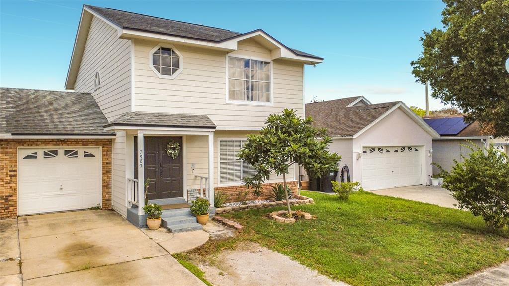 A two-story house with beige siding, a front porch, and two separate garage doors — 7987 SAGEBRUSH PLACE, ORLANDO, FL