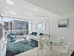 A bright living and dining area features a white sofa, glass tables, and floor-to-ceiling windows — 6801 Collins Ave, Miami Beach FL 33141, MIAMI BEACH, FL