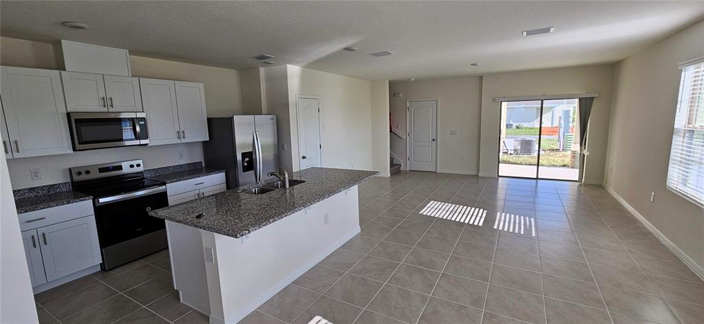 A kitchen with white cabinets, granite countertops, and stainless steel appliances opens to a living area — 1746 RED CANYON DRIVE, KISSIMMEE, FL