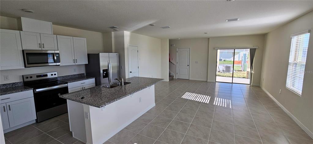 A kitchen with white cabinets and granite countertops opens into a tiled living area — 1746 RED CANYON DRIVE, KISSIMMEE, FL