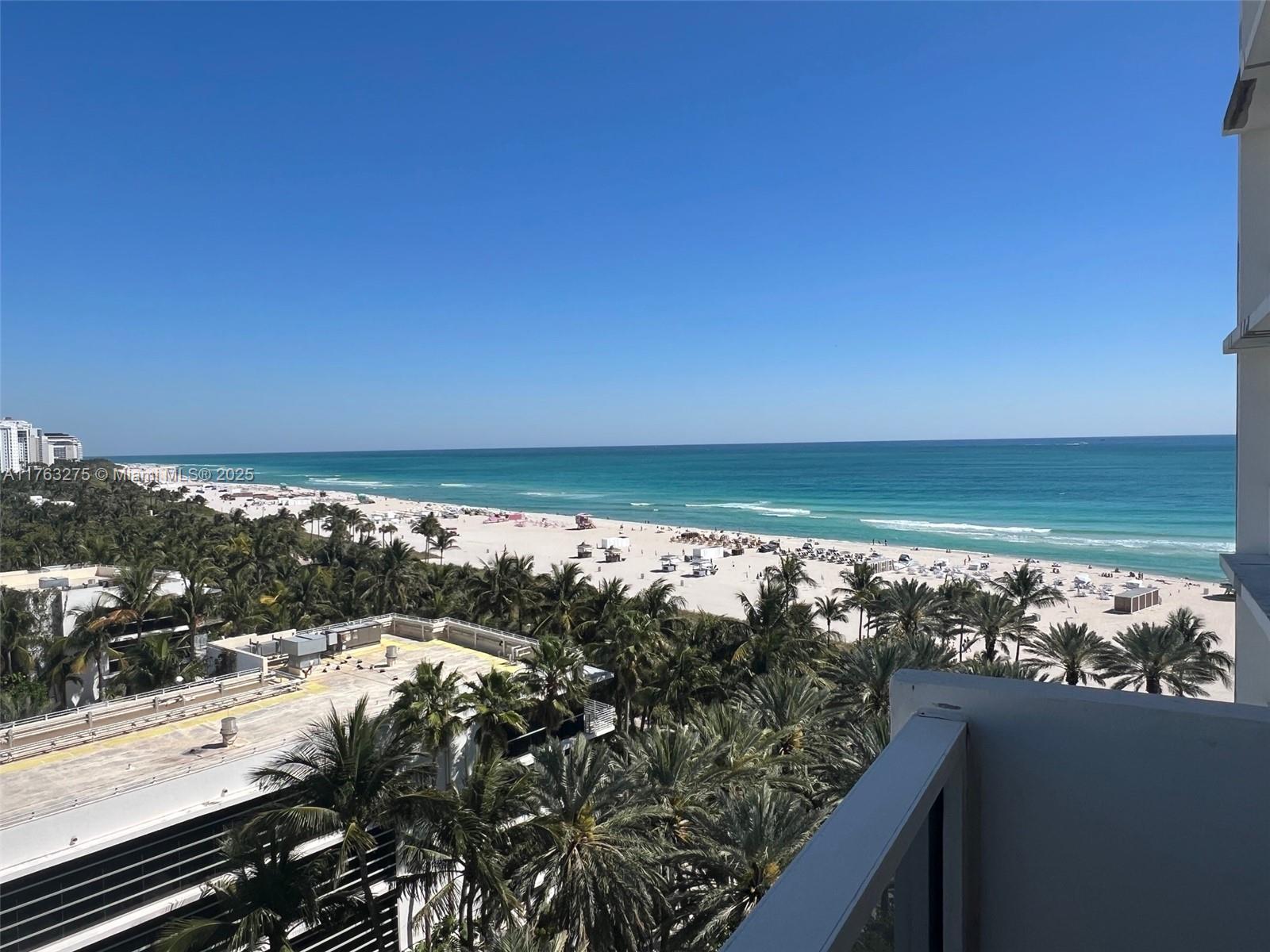 A high-angle view from a balcony overlooks a sandy beach, palm trees, and the ocean — 100 Lincoln Rd # 945, Miami Beach FL 33139, MIAMI BEACH, FL