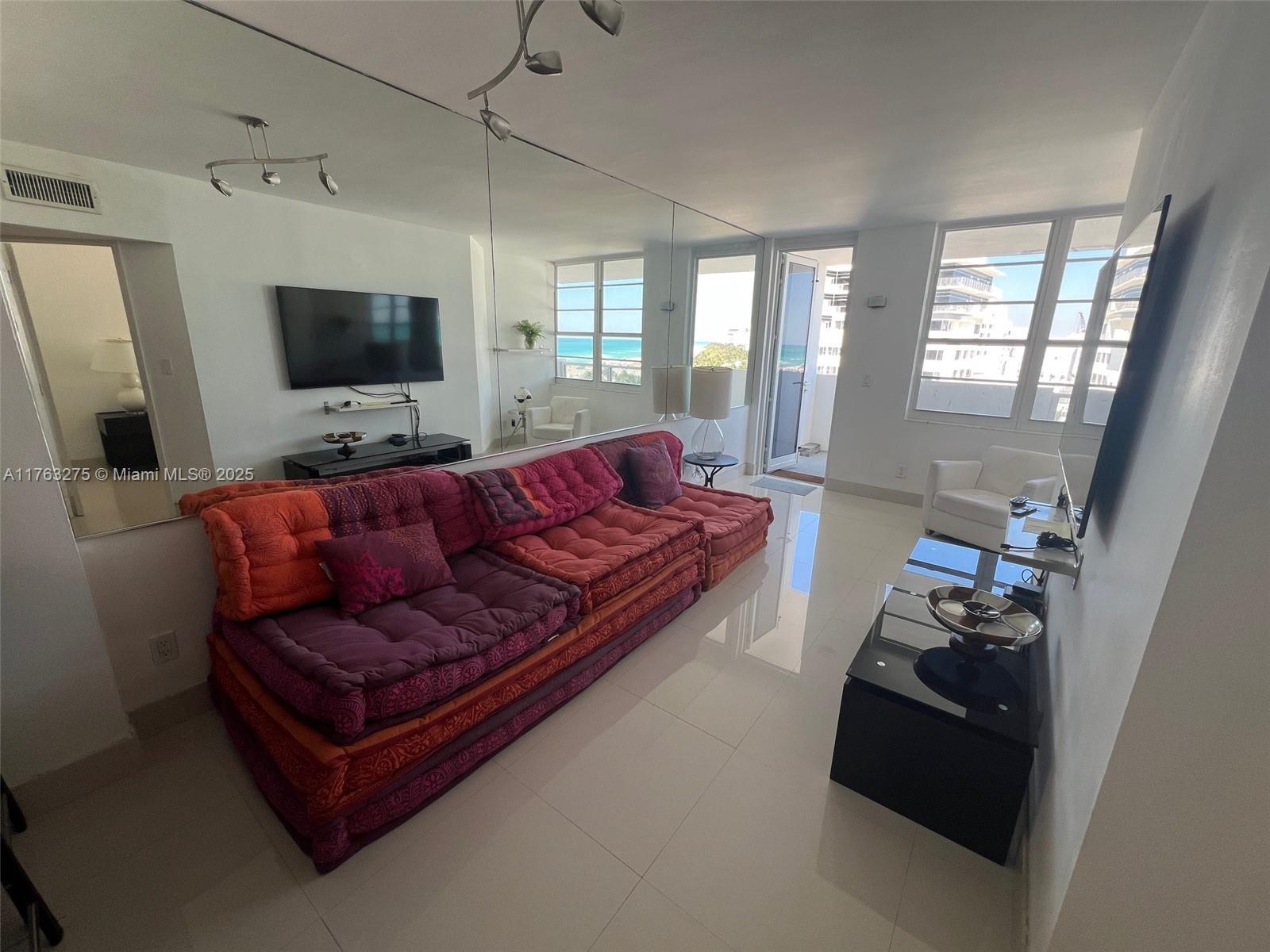 A living room features a large red sofa, mirrored walls, and a view of the ocean — 100 Lincoln Rd # 945, Miami Beach FL 33139, MIAMI BEACH, FL