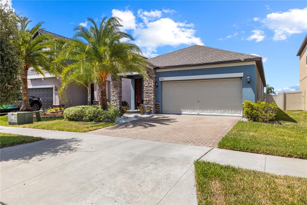 A single-story house with a blue exterior, stone accents, a two-car garage, and palm trees — 9611 IVORY DRIVE, SUN CITY CENTER, FL