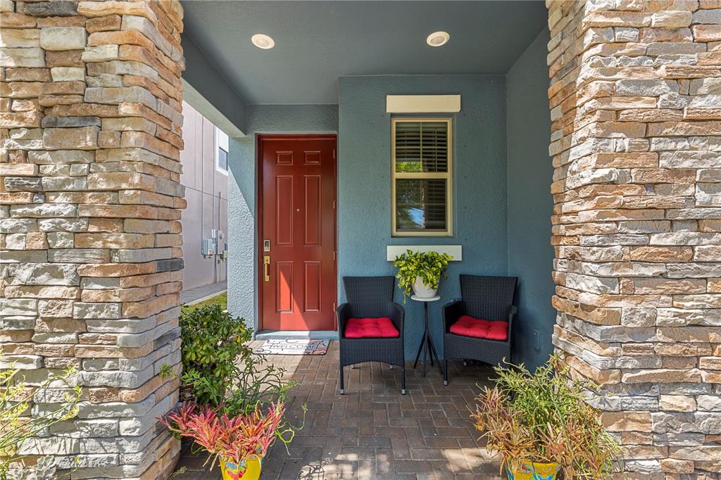 A front porch features a red door, two wicker chairs, and stone-clad support columns — 9611 IVORY DRIVE, SUN CITY CENTER, FL