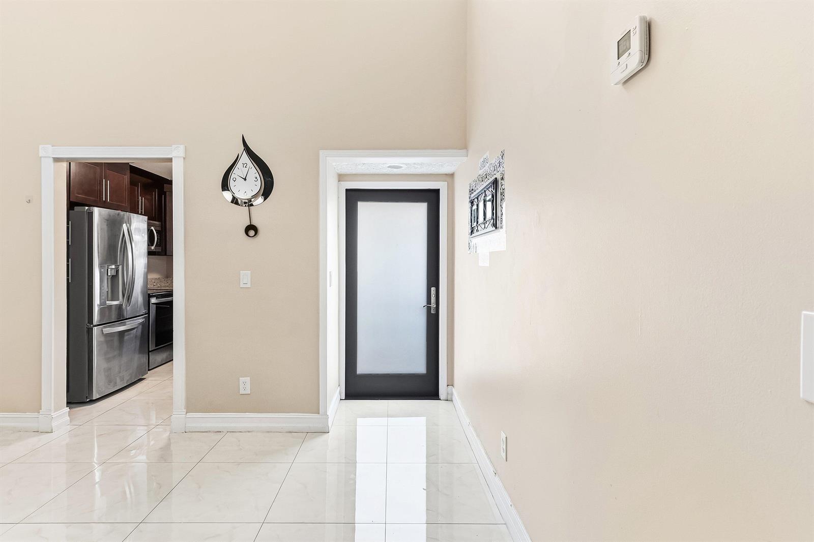 A room with white tiled floors, a dark-framed frosted glass door, and a wall clock — 1875 Abbey Road, West Palm Beach FL 33415, WEST PALM BEACH, FL