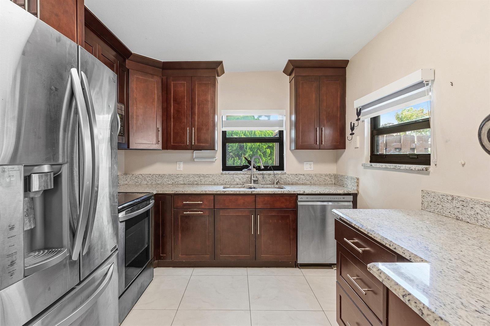 A kitchen features dark wood cabinets, granite countertops, stainless steel appliances, and light tile flooring — 1875 Abbey Road, West Palm Beach FL 33415, WEST PALM BEACH, FL