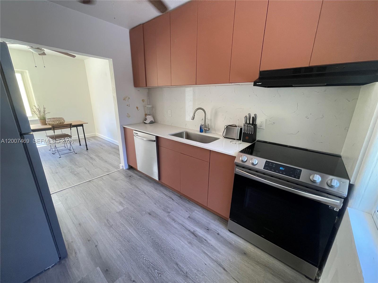 A kitchen features terracotta-colored cabinets, stainless steel appliances, and a white marble-patterned backsplash — FORT LAUDERDALE, FL