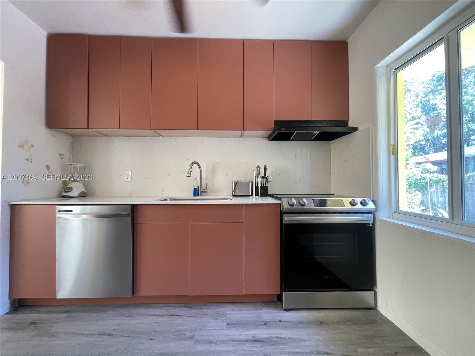A kitchen features terracotta-colored cabinets, stainless steel appliances, and a white marble-patterned backsplash — FORT LAUDERDALE, FL