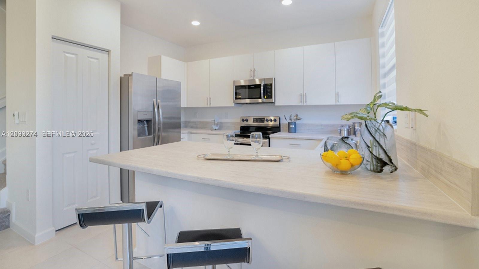 A modern kitchen features white cabinets, stainless steel appliances, and a light-colored breakfast bar — 2591 SE 26 CT, Homestead FL 33035, HOMESTEAD, FL