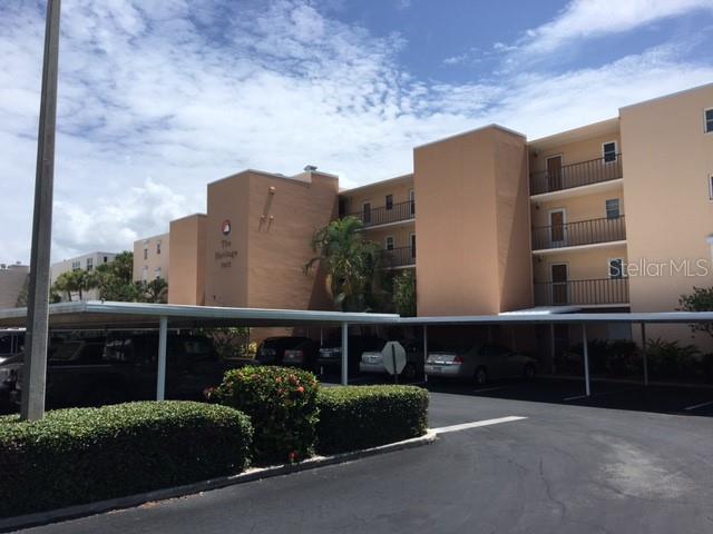 A multi-story apartment building with covered parking spaces and landscaped bushes in the foreground — 7625 SUN ISLAND DRIVE S UNIT 202, SOUTH PASADENA, FL