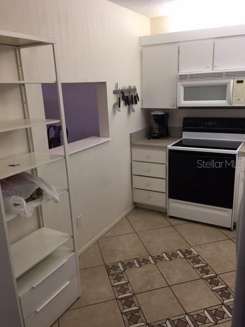 A kitchen features white cabinets, a black stove, a microwave, and a tall white shelving unit — 7625 SUN ISLAND DRIVE S UNIT 202, SOUTH PASADENA, FL