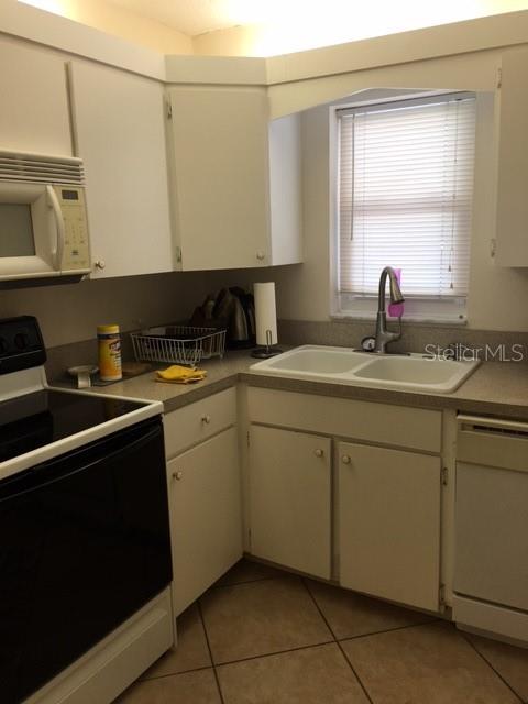 A kitchen features white cabinets, a double sink, a black stove, and tiled flooring — 7625 SUN ISLAND DRIVE S UNIT 202, SOUTH PASADENA, FL