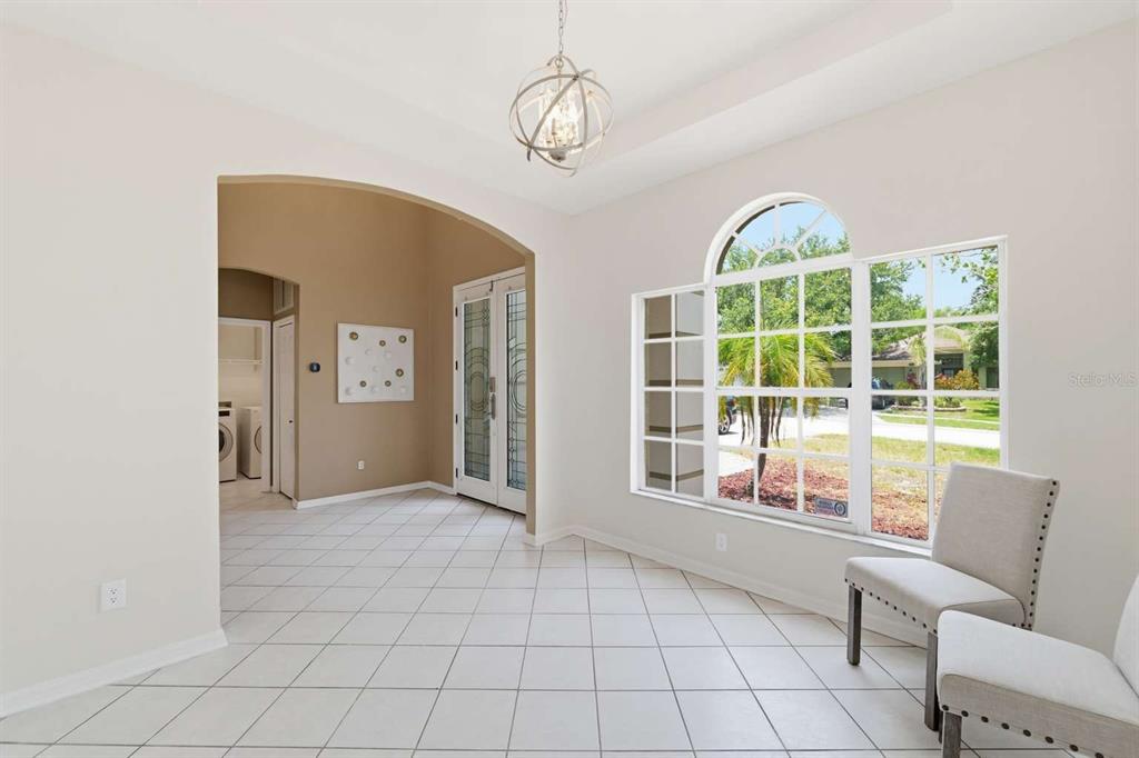 A bright dining room features tiled floors, a chandelier, and a large arched window — 1837 BRILAND STREET, TARPON SPRINGS, FL