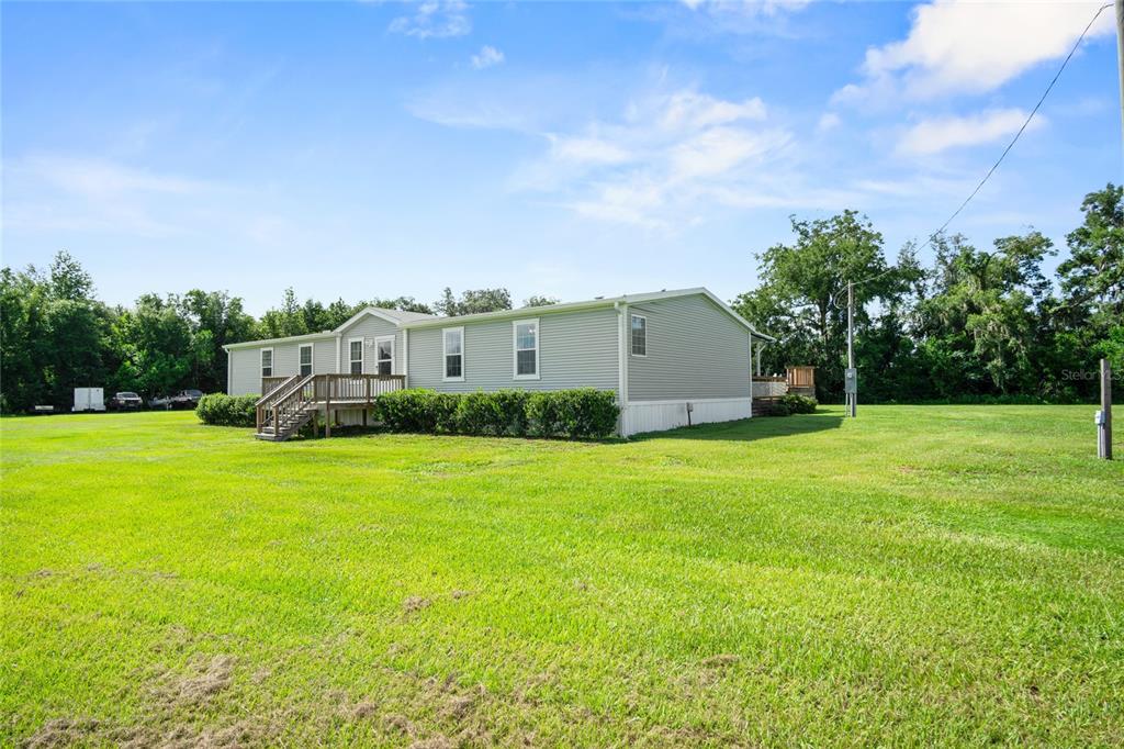 A light gray manufactured home sits on a large, grassy lot under a blue sky — 39670 WILDS RD, DADE CITY, FL