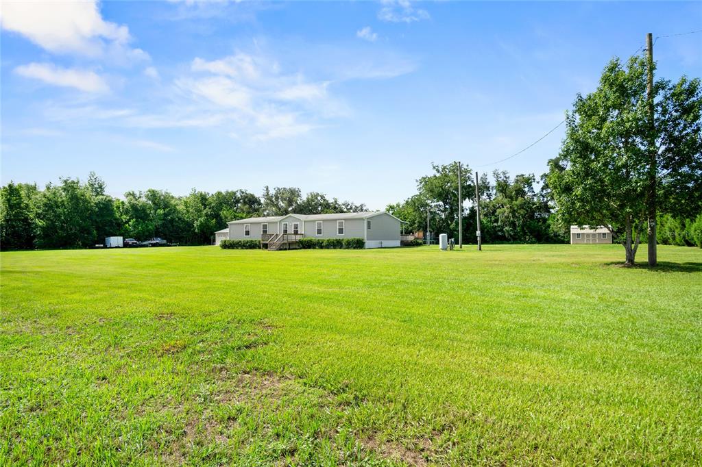 A wide, grassy field leads to a single-story manufactured home under a blue sky — 39670 WILDS RD, DADE CITY, FL