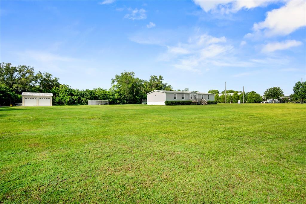 A wide, grassy field features a manufactured home and a detached garage under a blue sky — 39670 WILDS RD, DADE CITY, FL