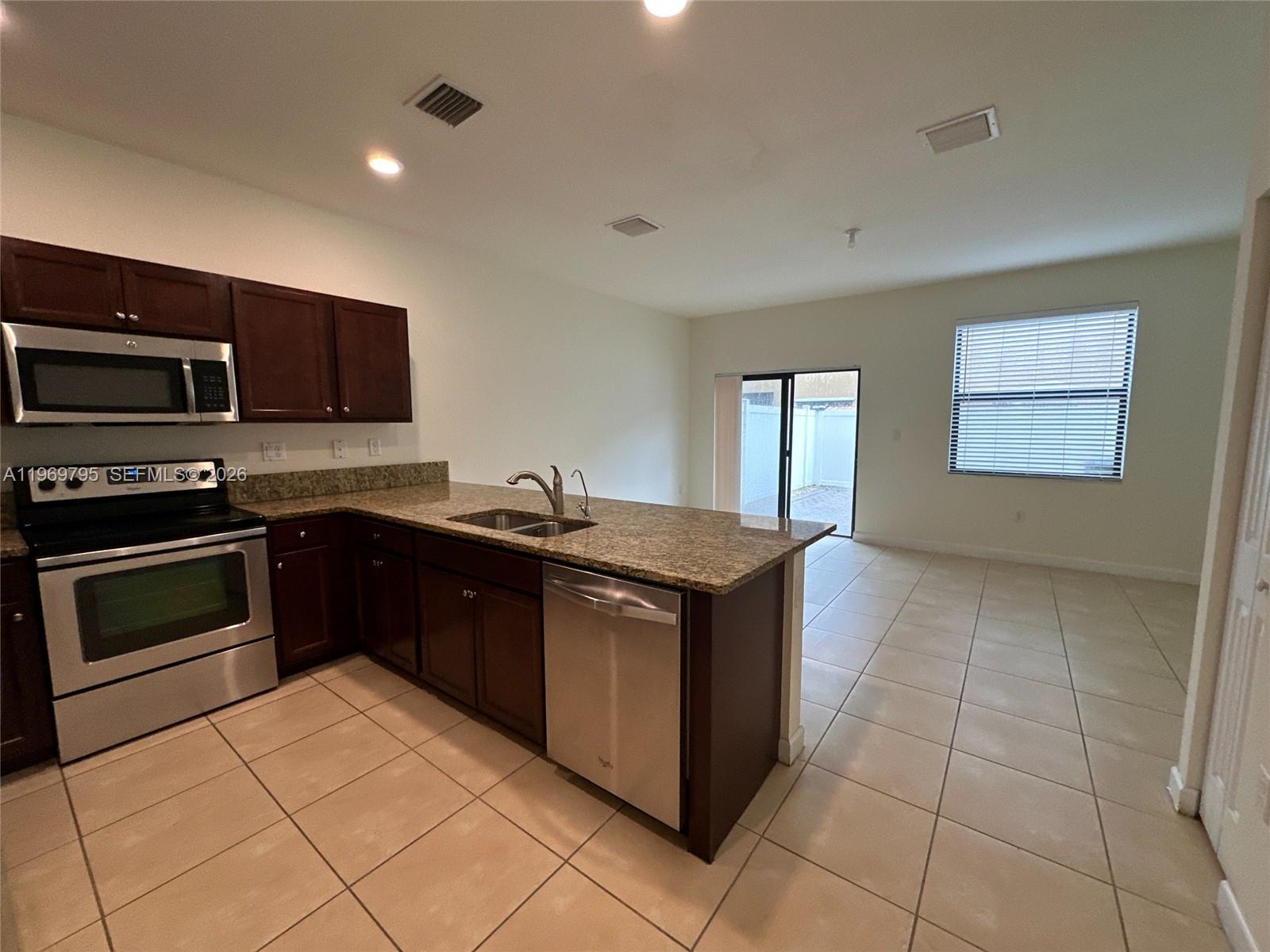 A kitchen with dark wood cabinets, granite countertops, and stainless steel appliances opens to a room — 9374 W 32nd Ln, Hialeah FL 33018, HIALEAH, FL