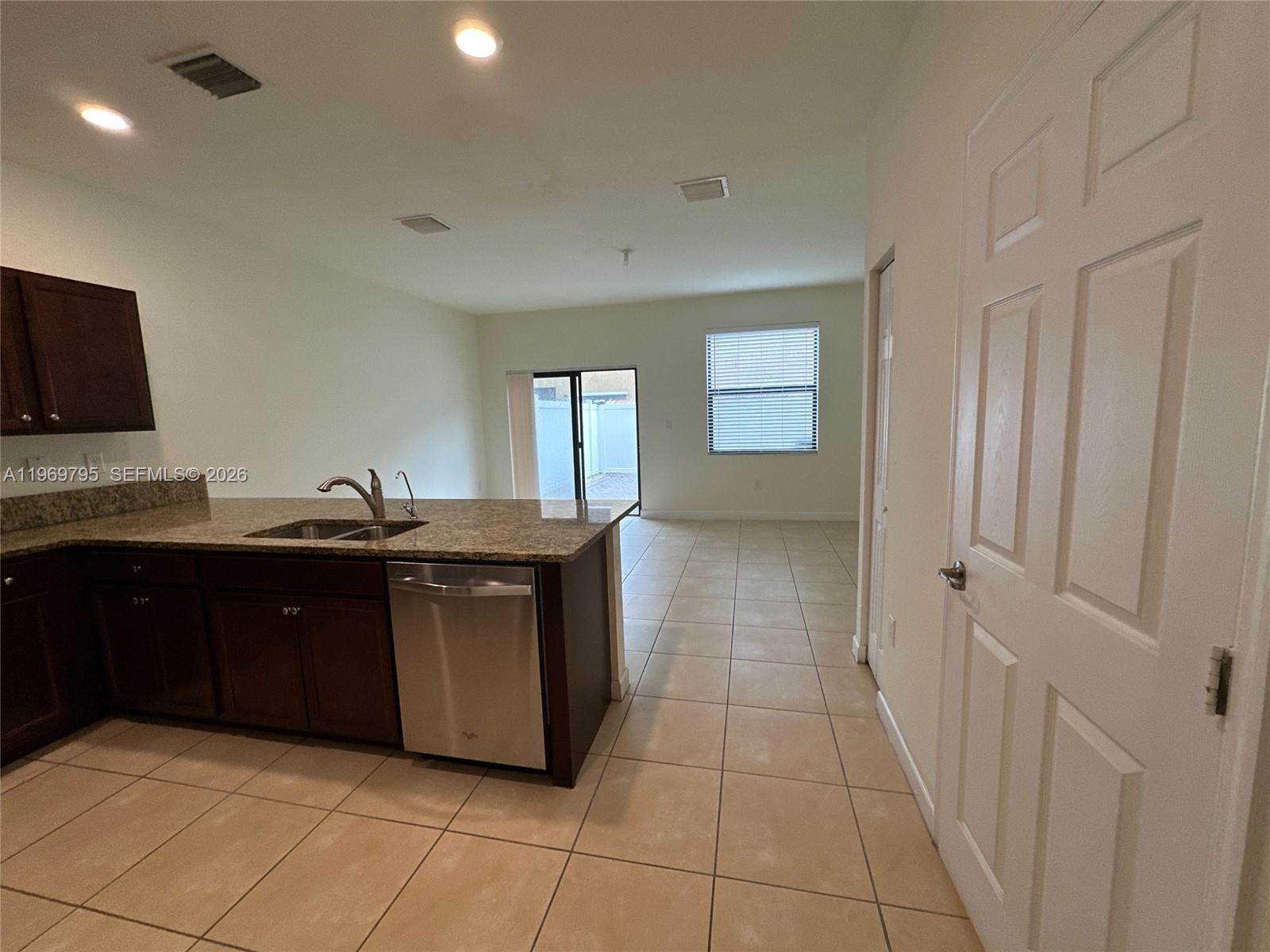 A kitchen with dark cabinets and granite countertops opens into a tiled living area — 9374 W 32nd Ln, Hialeah FL 33018, HIALEAH, FL