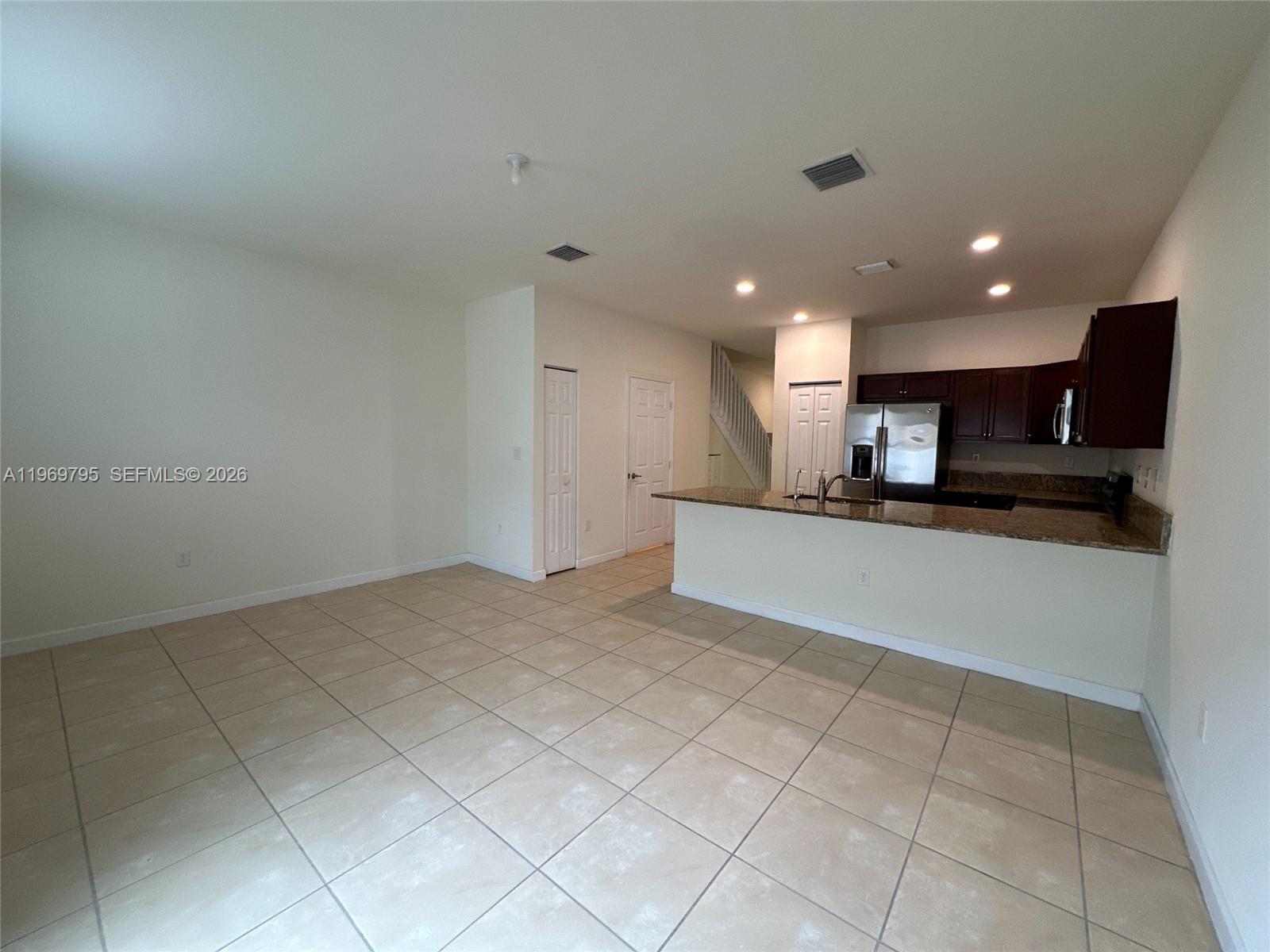An open-concept kitchen with dark cabinets and granite countertops overlooks a tiled living area — 9374 W 32nd Ln, Hialeah FL 33018, HIALEAH, FL