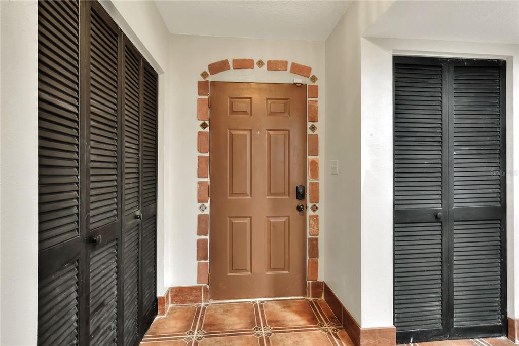 A brown front door is framed by decorative brickwork between two sets of black louvered doors — 1880 N CRYSTAL LAKE DRIVE UNIT 4, LAKELAND, FL