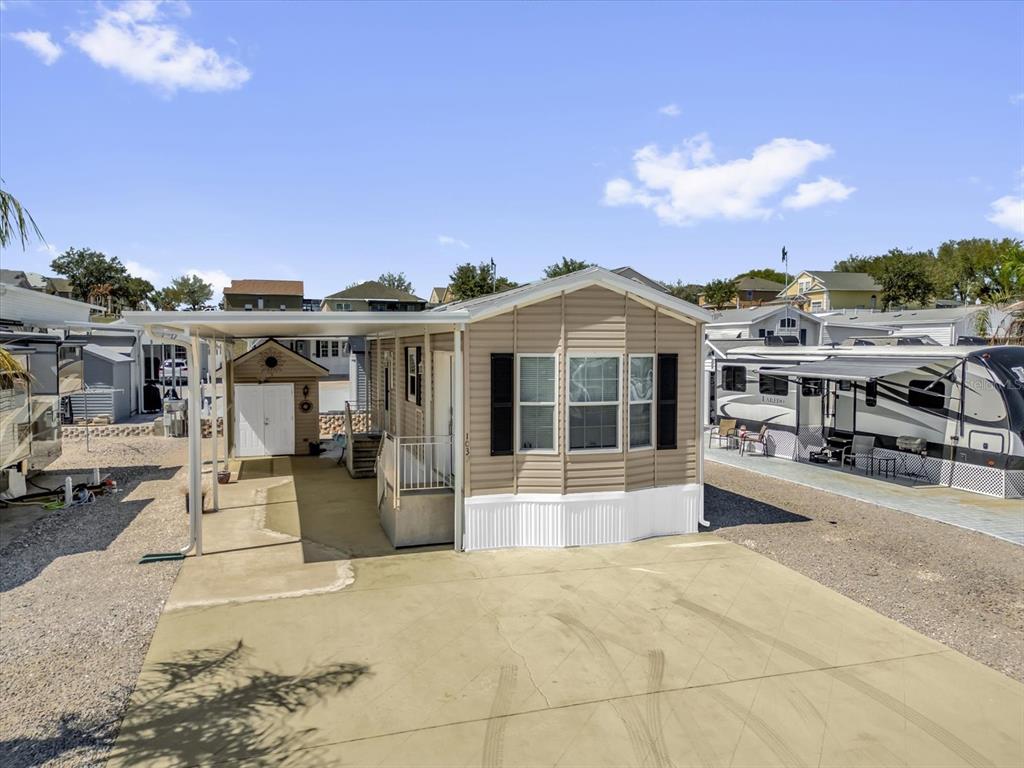 A tan mobile home with a carport and concrete driveway under a blue sky — 1039 CENTER CREST BOULEVARD, DAVENPORT, FL