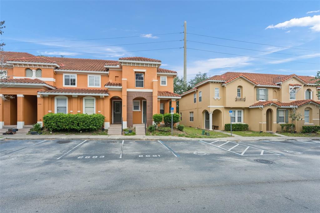 A two-story stucco townhouse complex with a parking lot in the foreground — 2691 ANDROS LANE, KISSIMMEE, FL