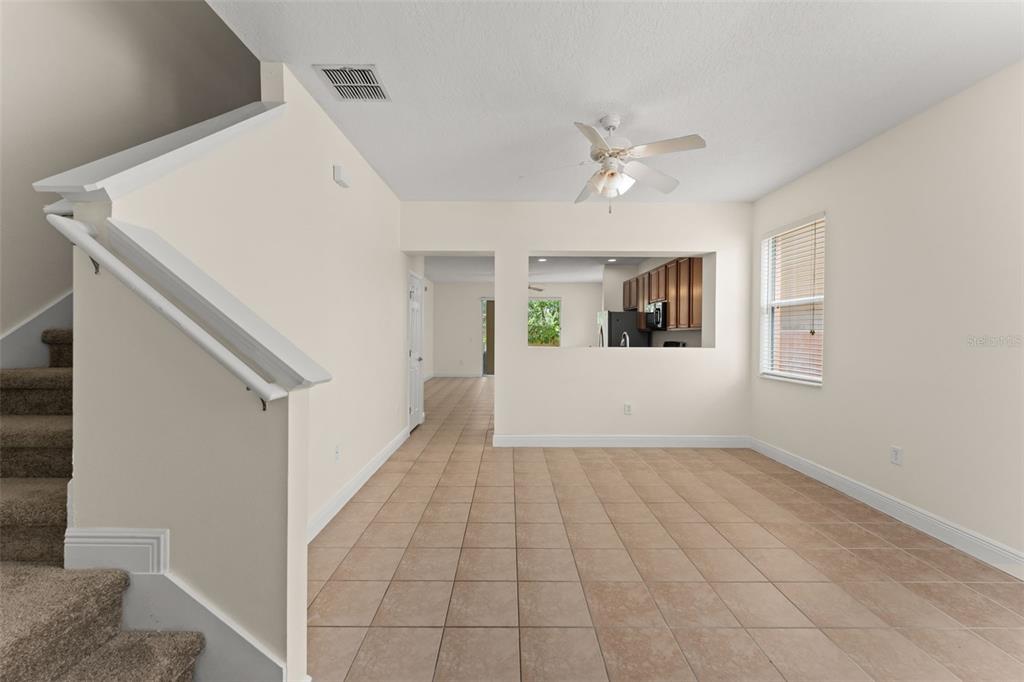 An interior view showing a tiled living area, a staircase, and a kitchen pass-through window — 2691 ANDROS LANE, KISSIMMEE, FL