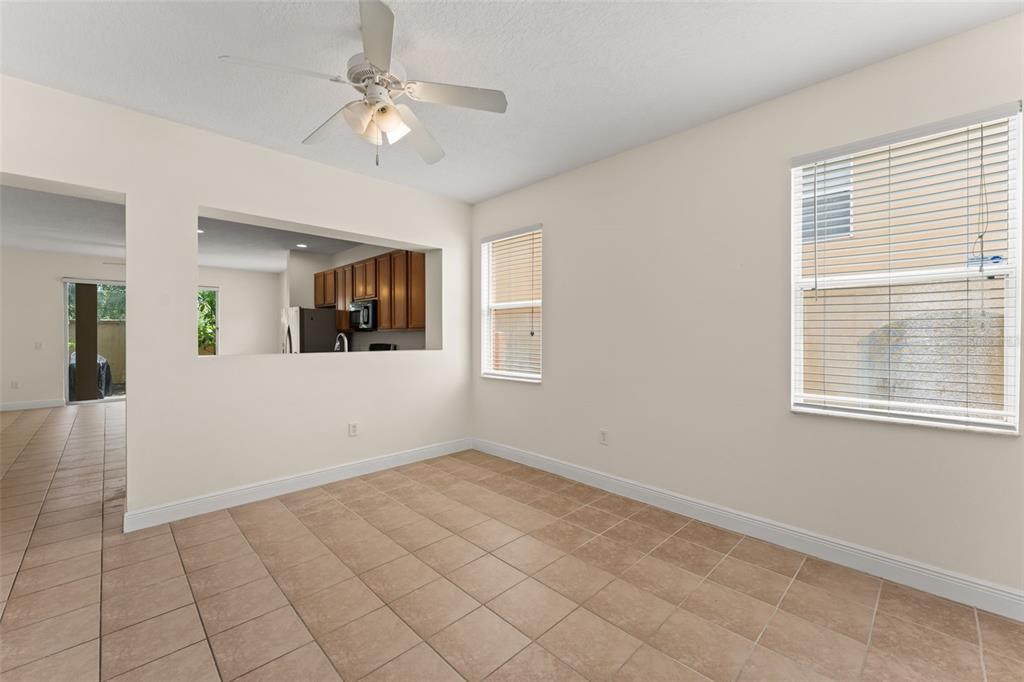 An empty dining area with beige tile flooring, a ceiling fan, and a kitchen pass-through window — 2691 ANDROS LANE, KISSIMMEE, FL