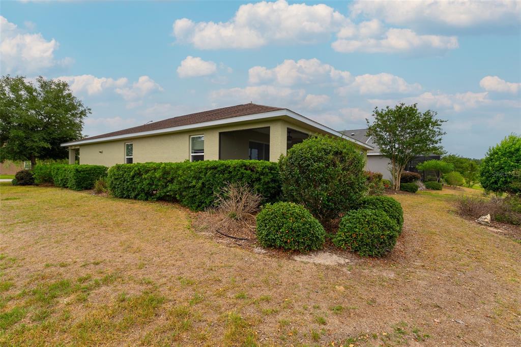 The exterior of a house features a screened-in porch, tan stucco walls, and landscaping — 10067 SW 89TH LOOP, OCALA, FL