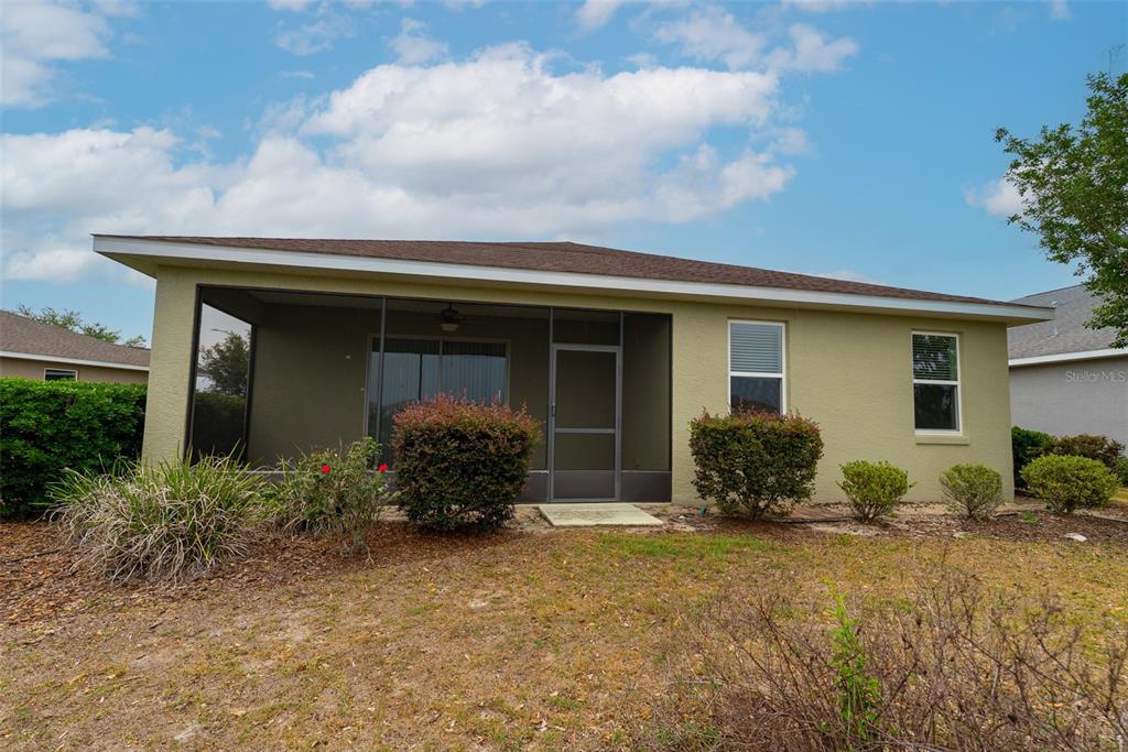 The exterior of a house features a screened-in patio, stucco walls, and a grassy yard — 10067 SW 89TH LOOP, OCALA, FL