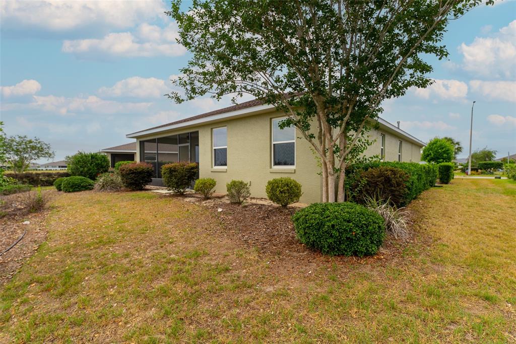 A side view of a tan house with a screened-in porch and landscaped bushes — 10067 SW 89TH LOOP, OCALA, FL