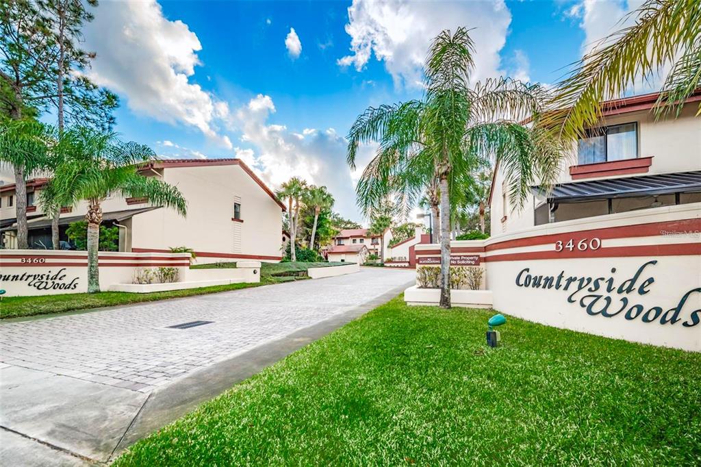 The entrance to a residential complex features a paved driveway flanked by two signs — 3460 COUNTRYSIDE #60 BOULEVARD, CLEARWATER, FL