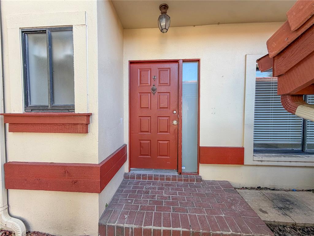 A red front door with a side window sits above a brick porch entrance — 3460 COUNTRYSIDE #60 BOULEVARD, CLEARWATER, FL